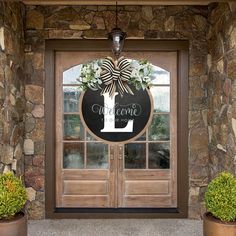 a welcome sign hanging on the front door of a house with two potted plants