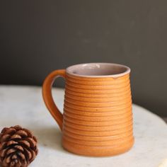 a ceramic mug with a pine cone on the side sitting on a marble table top