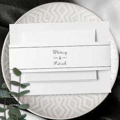 two place cards on a white plate with greenery in the middle and black text