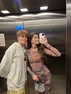 a man and woman taking a selfie in front of an elevator with their cell phone