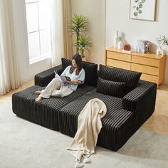 a woman sitting on top of a black couch next to a white carpeted floor