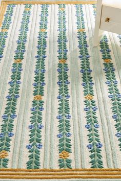 a white chair sitting on top of a rug covered in blue flowers and green leaves