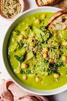 a white bowl filled with broccoli soup next to slices of bread and sprinkled nuts