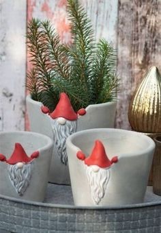 three white ceramic pots with red santa hats on them and pine branches in the background