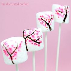 four lollipops decorated with pink and white cherry blossom designs on sticks in front of a pink background