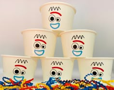 five cups with faces drawn on them and streamers around them, all decorated in different colors