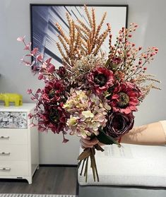 a person holding a bouquet of flowers in their hand on a bed with a painting behind them