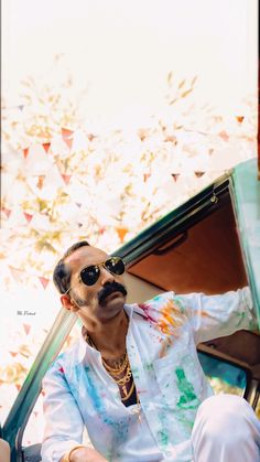 a man in sunglasses and tie dyes sitting on the back of a car with his hand out