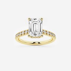 an emerald - cut engagement ring with diamonds on the band and side stones in yellow gold