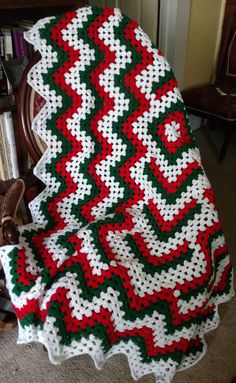 a crocheted afghan is sitting on the floor next to a chair and bookshelf