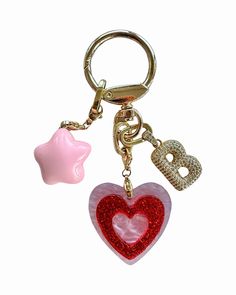 a heart shaped keychain with two charms attached to it's sides, one pink and one red