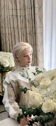 a woman with white hair sitting in front of a bouquet of roses and greenery