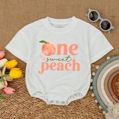 a white onesuit with the words one sweet peach printed on it next to flowers and sunglasses