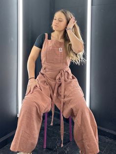 a woman sitting on top of a chair wearing overalls and holding her hair in the air