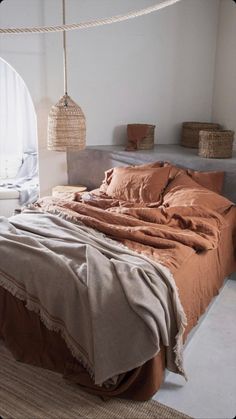 a bed with an orange comforter in a room next to some baskets and pillows