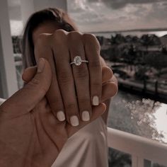 a woman holding up her engagement ring in front of the camera, with an ocean view behind her