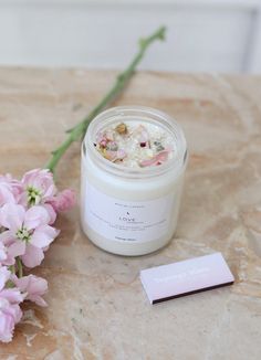 a candle and some pink flowers on a marble table with a business card next to it