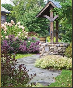 a stone and wood gazebo in the middle of a garden with flowers around it