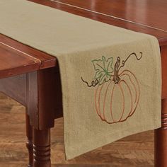 an embroidered table runner with a pumpkin on the front and leaves on the back, sitting on a wooden table