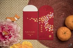 two oranges sitting on top of a table next to a red packet with flowers