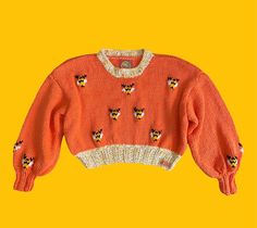 an orange sweater with cats on it is hanging from a yellow background and there is no image to describe