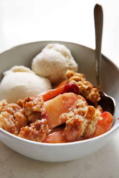 a bowl filled with fruit and ice cream on top of a white counter next to a spoon