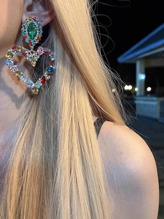 a woman with long blonde hair wearing large colorful earring set in front of her face