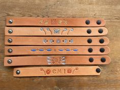 four leather nameplates with butterfly designs on them sitting on a wooden table next to each other