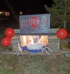 a creepy clown sitting in front of a fire place with balloons and a sign on it