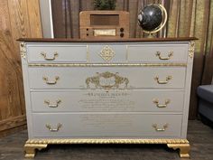 an old dresser with gold trim and writing on the drawers is displayed in front of a blue chair