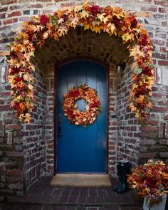 a blue door with a wreath on it and some fall leaves hanging over the doorway