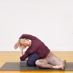 a woman sitting on top of a yoga mat with her hands behind her head while stretching