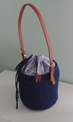 Navy Bucket Bag. Crocheted navy blue bucket bag, cotton blue and white fabric lining, inside pockets, drawstring closure, and brown leather buckle strap.  Dimensions: 23 inches round, 7.25 inches deep, 12 inch strap drop.  Surface washable.  Thank you for visiting YellowRoseRetail.com! Cotton Bucket Bag With Leather Handles, Blue Canvas Bucket Bag For Daily Use, Casual Blue Bucket Bag With Removable Pouch, Casual Blue Crossbody Bucket Bag, Blue Tote Bucket Bag, Blue Tote Bucket Bag With Handles, On-the-go Bucket Bag With Braided Handles, Blue Canvas Bucket Bag, Casual Blue Bucket Bag With Adjustable Strap