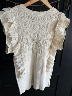 Gussy up your winter wardrobe with this romantic lace-trimmed sweater. The ivory design features ruffles and a delicate crochet lace trim, making for a look that's sure to turn heads. Sleeveless and cozy, you'll love this one-of-a-kind addition to your closet! True to size. Ruffled Knit Top For Layering, Ruffled Crew Neck Knit Top, Crew Neck Knit Top With Ruffles, Spring Knit Tops With Scalloped Edges, White Ruffled Sweater For Spring, Fall Lace Top With Ruffles, Chic Sleeveless Crochet Top With Ruffles, Beige Crochet Top With Lace Trim For Fall, Chic Ruffled Sweater For Layering