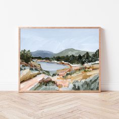 a painting on a wall with a wooden frame in front of it that has an image of a lake and mountains