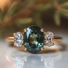 three stone ring with green and white stones on it's sides, sitting on a table