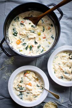 two bowls of chicken and dumpling soup with a wooden spoon in them on a gray cloth