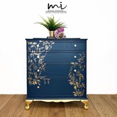 a blue and gold painted dresser with flowers on the top, in front of a white wall