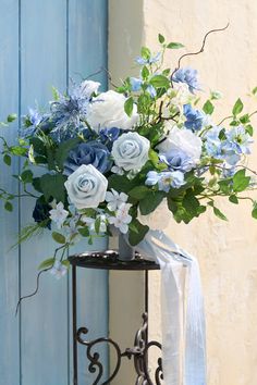 a vase filled with blue and white flowers sitting on top of a metal stand next to a wall