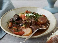 a white bowl filled with meat and carrots on top of a wooden table next to a glass of water