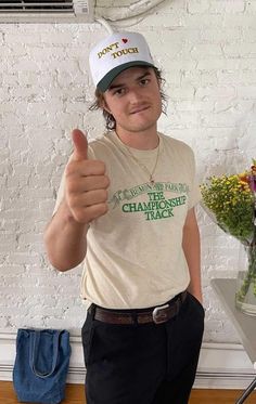 a man giving the thumbs up sign in front of a white brick wall with flowers