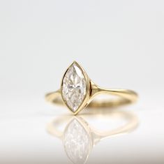 a yellow gold engagement ring with a pear shaped diamond in the center on a reflective surface