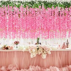 pink flowers hanging from the ceiling above a table with white and pink decorations on it