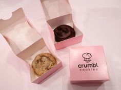 two pink boxes with cookies in them on a white tablecloth and one has an open box that says, crumbl cookies