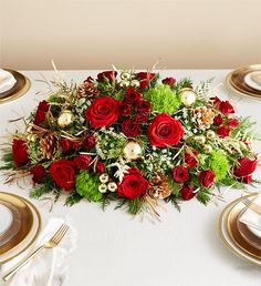 a bouquet of red roses sits on top of a white table cloth with gold place settings