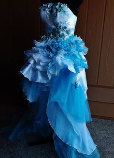 a blue and white dress with flowers on the skirt is displayed in front of a wooden wall