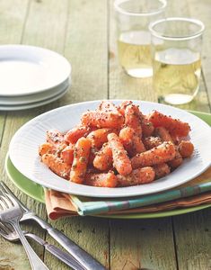 a white plate topped with fried carrots on top of a wooden table next to silverware