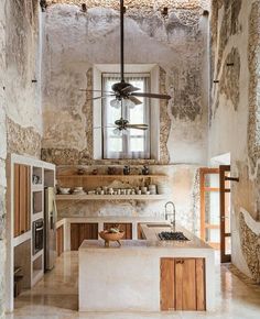 a kitchen with an island counter and ceiling fan in the middle, surrounded by stone walls