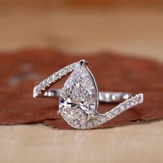 a pear shaped diamond engagement ring on top of a wooden surface with leaves around it