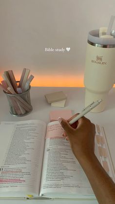 a person holding a pen and writing on a book next to a cup with pencils in it